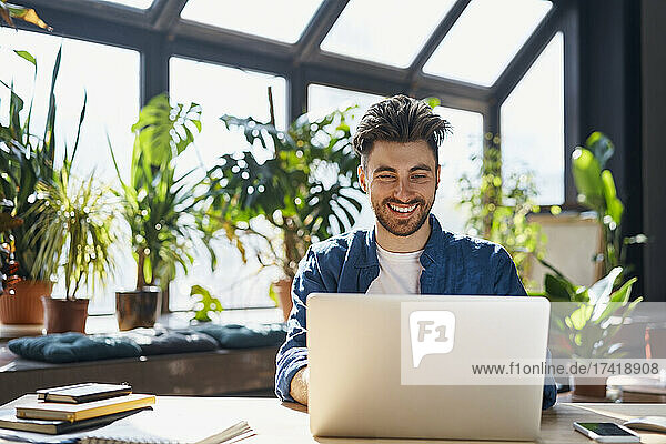 Happy male professional using laptop while sitting at desk in office