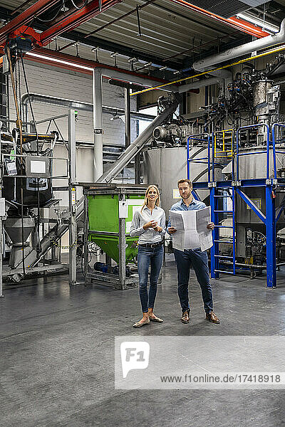 Male and female coworkers with business plan standing at industry