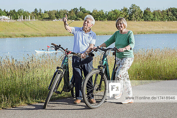 Älterer Mann zeigt  während er mit Frau spricht  die neben Fahrrädern steht