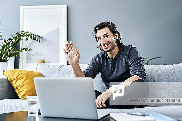 Businessman waving during video call on laptop at home