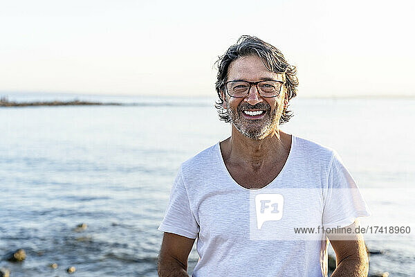 Happy mature man wearing eyeglasses at beach during sunset