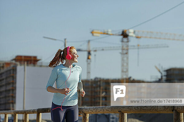 Smiling woman jogging near construction site during sunny day