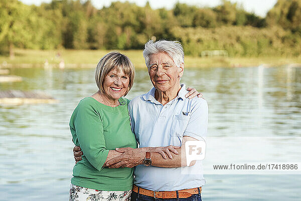 Smiling senior couple standing with arm around at lake