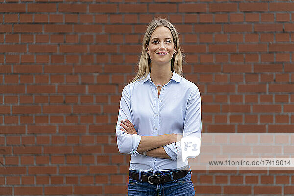 Smiling businesswoman with arms crossed standing in front of wall