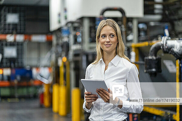 Smiling businesswoman with digital tablet standing at factory