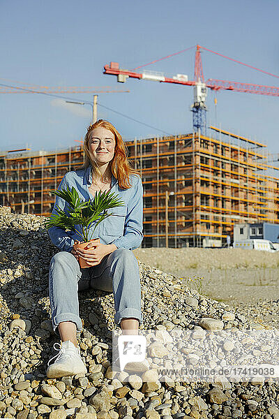 Young woman sitting with potted plant on pile during sunny day