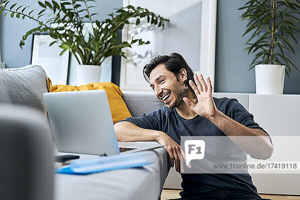 Businessman waving while doing video call on laptop at home