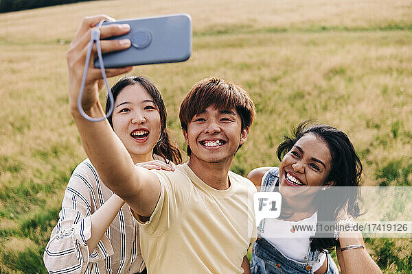 Friends smiling while taking selfie through mobile phone at park