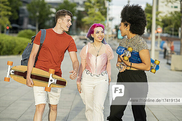 Multiethnische männliche und weibliche Freunde reden miteinander  während sie auf dem Fußweg gehen