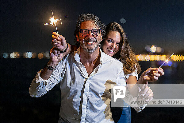 Vater und Tochter halten nachts Wunderkerzen in der Hand