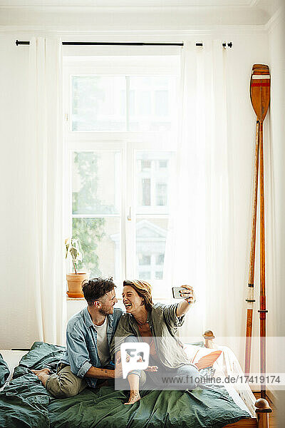 Glückliches Paar macht ein Selfie  während es zu Hause im Bett sitzt