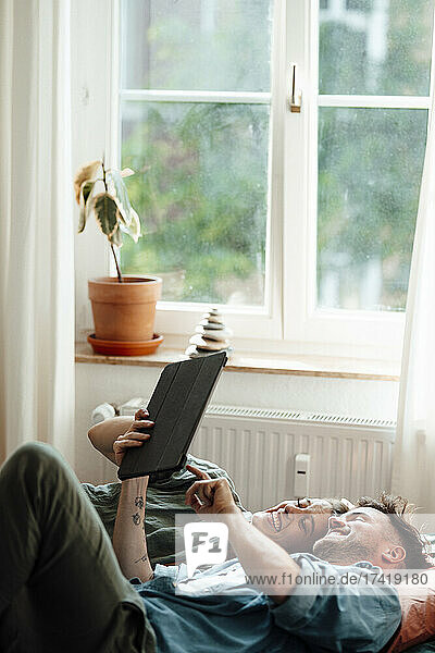 Cheerful couple with digital tablet lying on bed at home