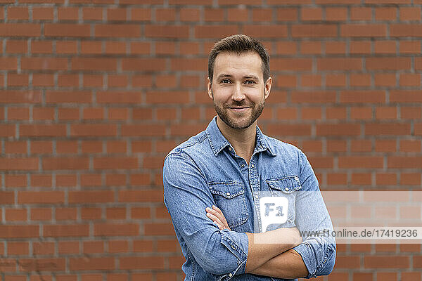 Happy businessman with arms crossed in front of wall