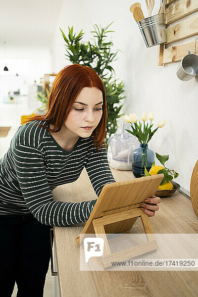 Redhead woman using digital tablet while leaning on kitchen counter