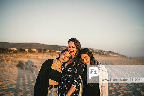 Smiling daughters leaning on shoulder of mother at beach