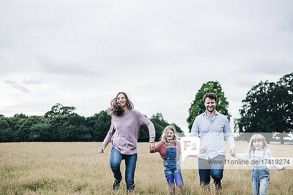 Happy family holding hands while running on meadow