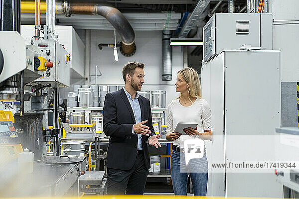 Businesswoman with digital tablet listening to manager while standing in factory