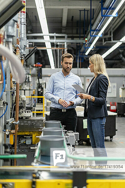 Female manager with digital tablet standing by colleague in factory