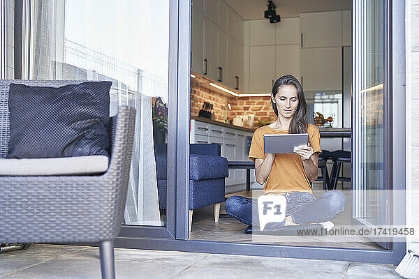 Frau sitzt mit gekreuzten Beinen vor der Tür und benutzt ein digitales Tablet