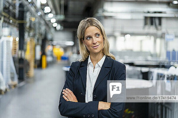 Thoughtful female manager with arms crossed in factory