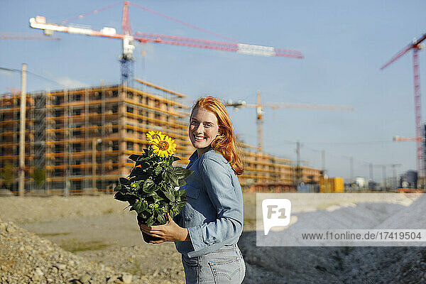 Lächelnde Frau mit blühender Pflanze steht auf der Baustelle