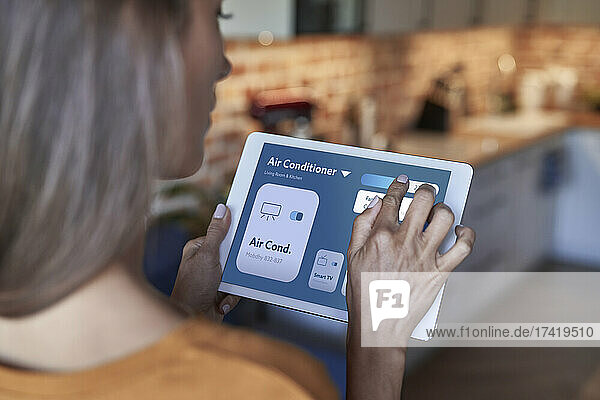 Woman adjusting air conditioner through digital tablet at home