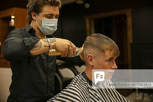 Männlicher Friseur schneidet während einer Pandemie einem Teenager im Friseurladen die Haare