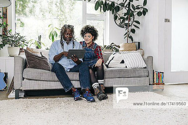 Senior man using digital tablet while sitting with daughter on sofa