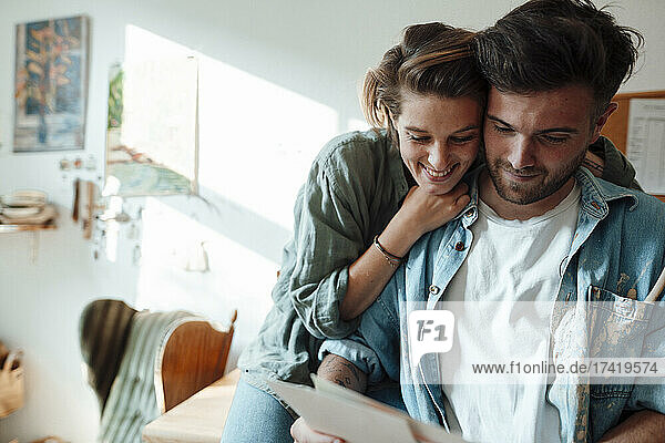 Woman embracing man while looking at document at home