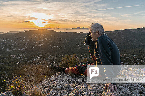 Senior man with head in hand sitting at cliff during hiking
