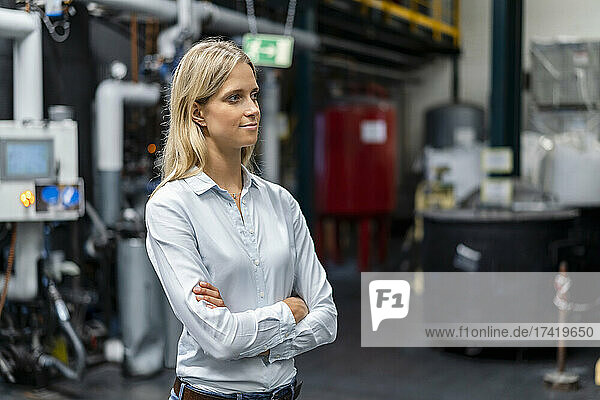 Thoughtful businesswoman with arms crossed in factory