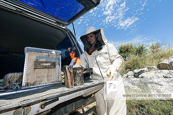 Female beekeeper burning bee smoker at car trunk