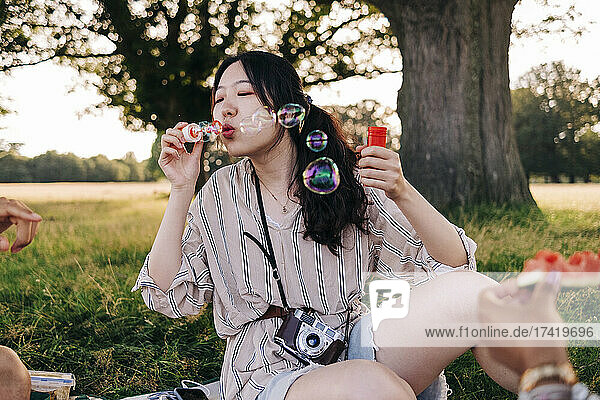 Woman blowing bubbles while sitting with friends at park