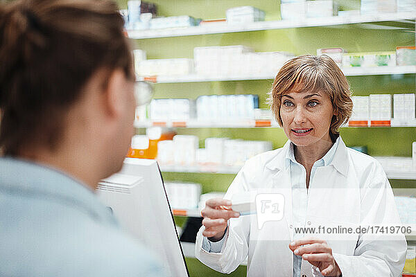 Female pharmacist explaining customer over medicine in pharmacy