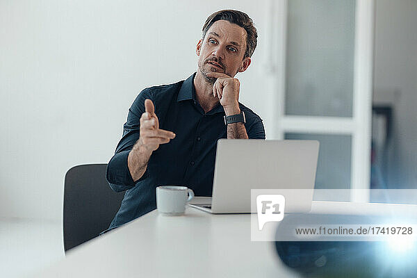 Mature businessman with laptop gesturing while talking in board room
