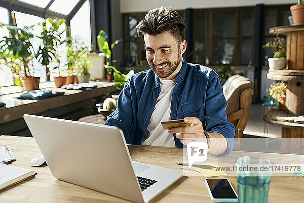 Männlicher Berufstätiger mit Kreditkarte beim Online-Shopping im Büro