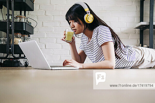 Woman drinking smoothie while using laptop at home