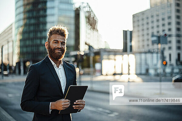 Smiling mature businessman with digital tablet standing on street