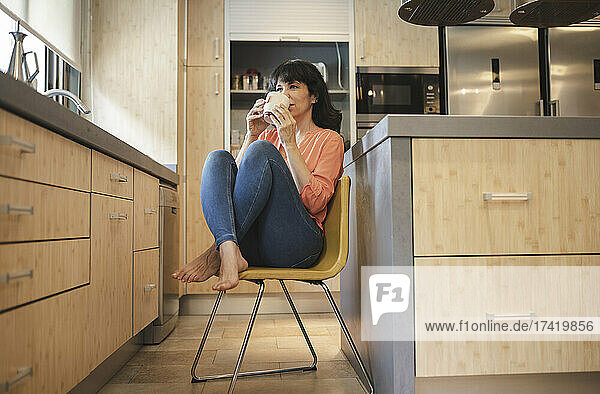 Reife Frau trinkt Kaffee  während sie zu Hause auf einem Stuhl in der Küche sitzt