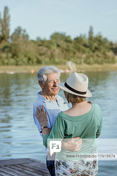 Senior man looking at woman wearing hat on jetty by lake