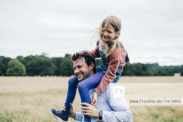 Smiling man carrying girl on shoulder while playing at meadow