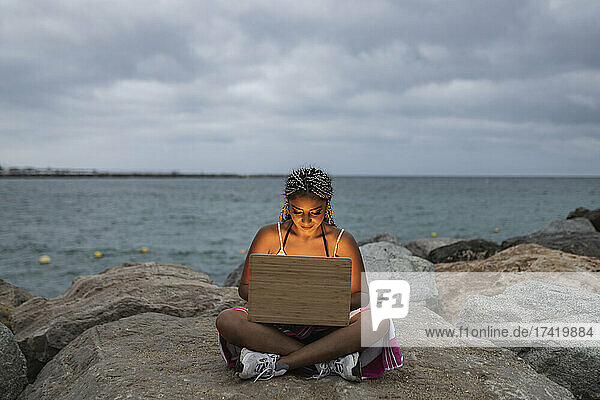 Woman using laptop on rock during sunset