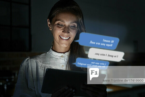 Smiling woman using smart phone at home during night