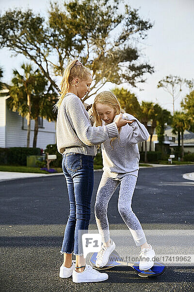 Girl helping female friend standing on skateboard