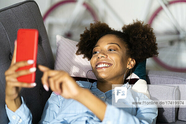 Afro-junge Frau benutzt Smartphone auf Sofa zu Hause