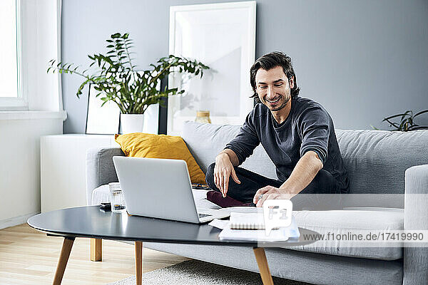 Lächelnder männlicher Profi  der arbeitet  während er zu Hause auf dem Sofa sitzt