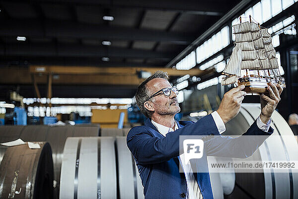 Businessman holding sailboat toy at steel mill