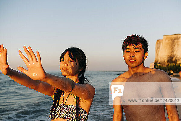 Young man standing by woman gesturing at beach during vacation
