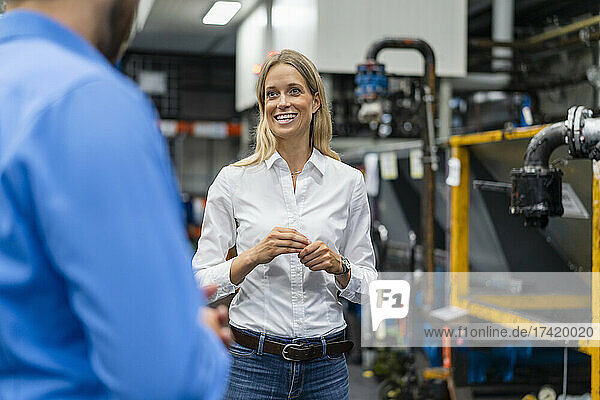 Smiling businesswoman discussing with colleague while standing in factory