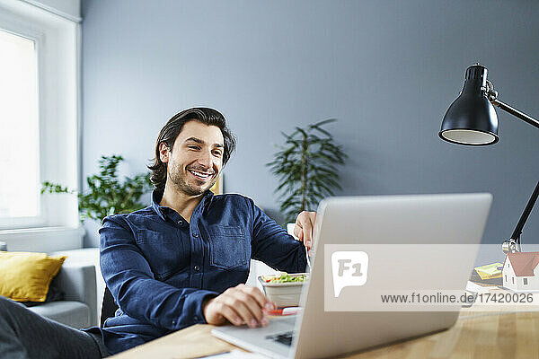 Smiling businessman using laptop at desk while sitting in office